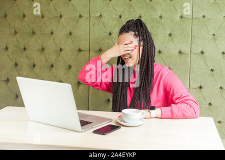 Ritratto di emozionale spaventato o sconvolto giovane imprenditrice con il nero dreadlocks acconciatura in rosa camicetta in seduta cafe e coprendo i suoi occhi e d Foto Stock