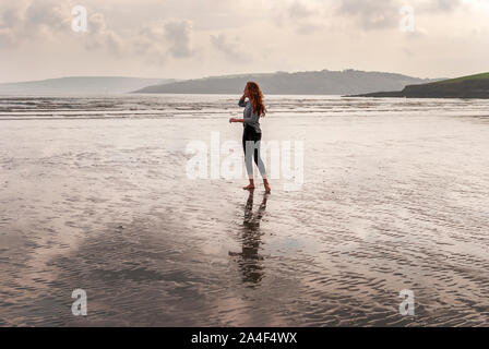 I giovani i Capelli rossi ragazza camminare sulla spiaggia di sabbia lasciando tracce nella sabbia. Giorno nuvoloso. Foto Stock