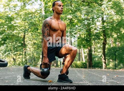 L'uomo esercita con kettlebell all'esterno. Atleta facendo squat utilizzando kettlebells. Foto Stock