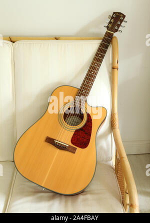 Un parafango chitarra acustica su un divano di vimini. Foto Stock