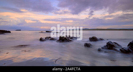 Malva tramonto con nuvole wispy sulla spiaggia Pollan, Inishowen, Irlanda. Dotate di rocce di alghe e sabbia con vista di Malin penisola sull orizzonte Foto Stock