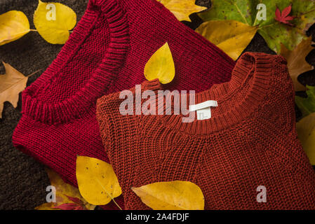 Moda laici piana di due coloratissimi caldo, lanugine, lana / Lana, accogliente maglioni / ponticelli su un autunnale di / autunno sfondo di giallo e rosso caduta foglie Foto Stock