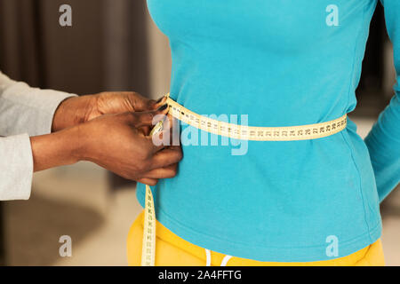 Designer di sesso femminile con le mani in mano la misurazione della donna di vita in abiti Atelier, Primo Piano Foto Stock