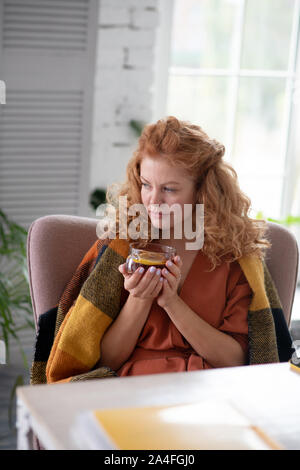 Donna con plaid sulle spalle bere il tè mentre avente la tosse Foto Stock