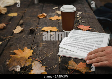 Femmina Maschio legge un libro in autunno park bevande da asporto caffè caffè. Close-up sulla spalla, sfocata. top view, consente di risparmiare spazio. Visto mani. In un oscuro Foto Stock