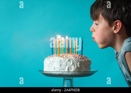 Ragazzo soffiando fuori candele su una torta di compleanno contro sfondo blu. Foto Stock