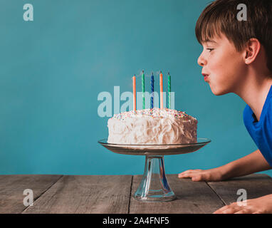 Ragazzo soffiando fuori candele su una torta di compleanno contro sfondo blu. Foto Stock