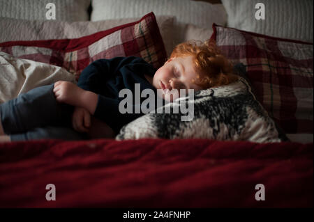 Il Toddler boy 1-2 anni addormentato su cuscini nel letto con lenzuola rosse Foto Stock