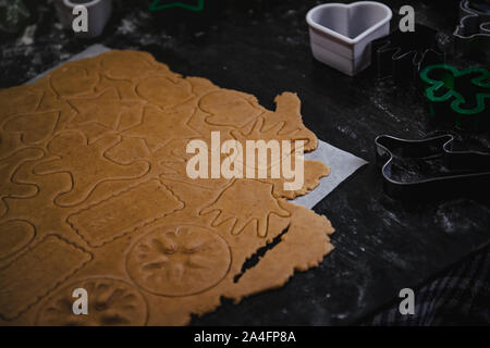 Tagliare gingerbread cookie nella forma di un albero di Natale, stella piccolo uomo, cuori da impasto crudo su pergamena carta da forno su uno sfondo scuro Foto Stock