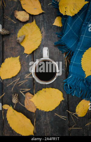 Su un vecchio tavolo di legno in autunno park è una tazza di tè e caffè. Un caldo blu plaid sciarpa è diffusa con foglie di giallo e pigne. Vista superiore Foto Stock