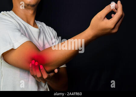 Uomo asiatico tenendo la sua mano. Egli si sente dolore sul suo gomito con sfondo nero. Medico o il concetto di assistenza sanitaria Foto Stock