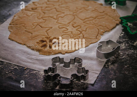 Tagliare gingerbread cookie nella forma di un albero di Natale, stella piccolo uomo, cuori da impasto crudo su pergamena carta da forno su uno sfondo scuro Foto Stock