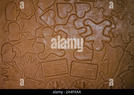 Tagliare gingerbread cookie nella forma di un albero di Natale, stella piccolo uomo, cuori da impasto crudo su pergamena carta da forno su uno sfondo scuro Foto Stock