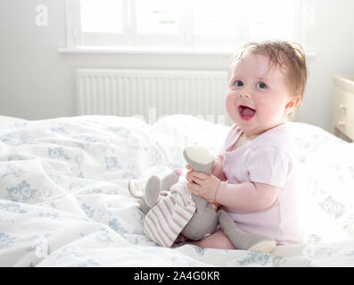 Il bambino seduto sul letto a sorridere per la fotocamera Foto Stock