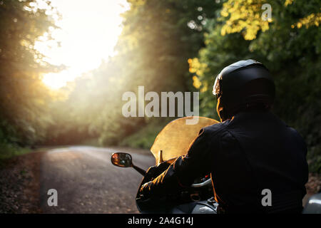 Biker con la sua motocicletta su strada, la preparazione per la corsa. Motociclo guy con la motocicletta sulla strada. Conducente del motociclo di equitazione sulla strada attraverso Foto Stock