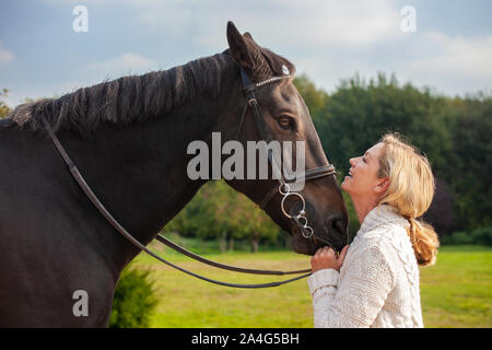 Felice bella donna di mezza età ridere, sorridente e tenendo premuto il suo cavallo vicino al sole Foto Stock