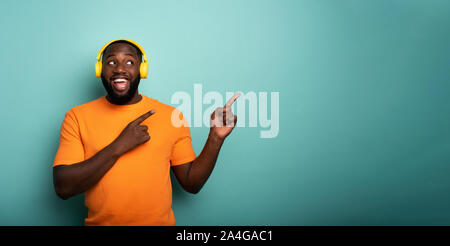 Ragazzo con auricolare giallo ascolta musica e indica qualcosa di Foto Stock