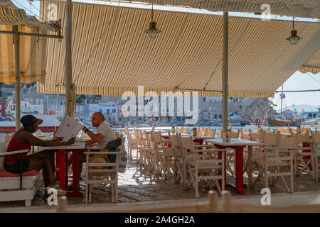 Hydra, isola greca - 20 luglio 2019; due persone sfocati al Waterfront Restaurant sull isola greca seduti ai tavoli sotto la tenda con focus su view Foto Stock