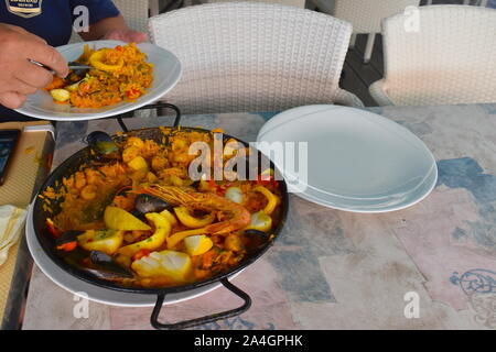 La paella di frutti di mare su un tavolo in un ristorante sul mare. Risotto di scampi, cozze, vongole, calamari, il pesce e i peperoni in un tradizionale rotondo di metallo pot. Foto Stock