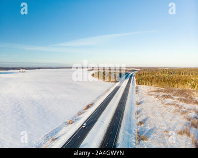 Bella vista aerea della coperta di neve i campi con una strada a due corsie tra gli alberi. Rime ghiaccio e gelo trasformata per forte gradiente di alberi di copertura. Scenic paesaggio invernale nei pressi di vi Foto Stock