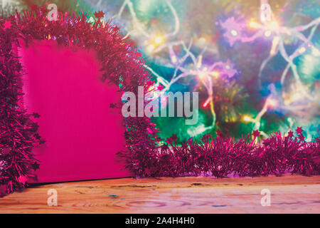 Un big red Natale desiderano prenotare decorata con una ghirlanda di fiori su un tavolo di legno contro l'albero di Natale. Una lettura del blocco note di cuoio - un regalo per Natale o Foto Stock