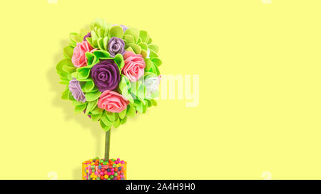 Bouquet di rose con foglie di colore verde con fatti a mano in plastica schiumosa con forma rotonda piantato in un vaso di vetro con le palle colorate su sfondo giallo con co Foto Stock