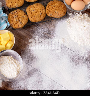 Appena sfornati i biscotti al cioccolato al buio su un tavolo di legno con spolverata di farina e ingredienti. Foto Stock