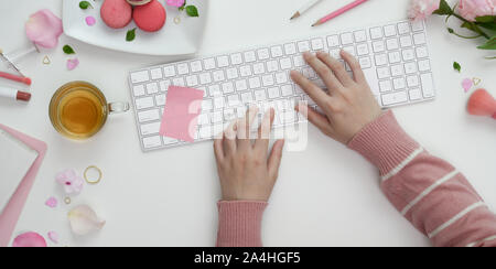 Vista superiore del giovane ragazza la digitazione sulla tastiera in dolce rosa area di lavoro femminile con il make up e delle forniture di ufficio Foto Stock