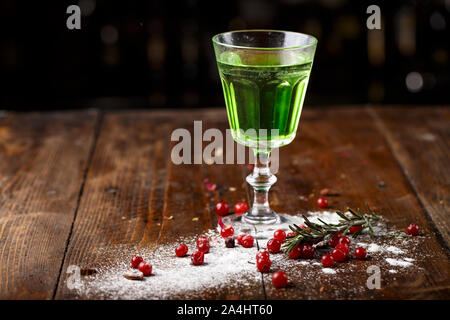 Cocktail verde sulla base di assenzio in un elegante vintage vetro su di un legno marrone. sfondo dello zucchero bianco e mirtilli sono sparsi nei dintorni Foto Stock