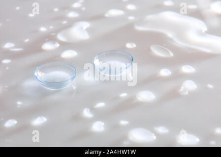 Lenti a contatto su vetro bianco tavola riflettente con gocce d'acqua. Composizione orizzontale. Vista in elevazione. Foto Stock