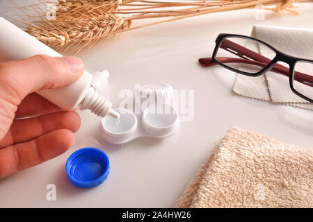 La mano di riempimento di una custodia per lenti a contatto con un flacone di soluzione. Composizione orizzontale. Vista in elevazione. Foto Stock