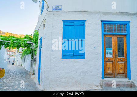 Hydra, isola greca - 20 luglio 2019; Edificio corrner su due corsie, whitwashed con porta blu e otturatore e vista lungo la pietra ciottoli sulla corsia di sinistra. Foto Stock