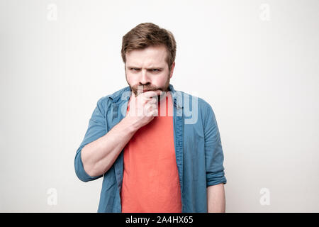 Malinconici uomo tocca il suo mento barbuto con la sua mano e guarda severamente la fotocamera a. Isolato su sfondo bianco. Foto Stock