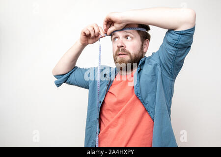 Una curiosa, uomo barbuto misure diametro della sua testa, con un grave aspetto. Isolato su sfondo bianco. Foto Stock