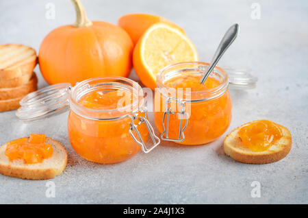 In casa di zucca e confettura di arancione in vasi su un cemento grigio Sfondo. Foto Stock