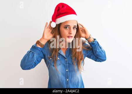 Giovani belle redhead donna con cappello a Natale su sfondo isolato cercando di ascoltare entrambe le mani sul gesto dell'orecchio, curiosi di gossip. Audizione pro Foto Stock