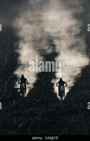 Due amici corrono su motocicli neri da corsa in stile retrò personalizzati sulla sabbia lavica nera all'alba sul monte Batur, Bali, Indonesia Foto Stock