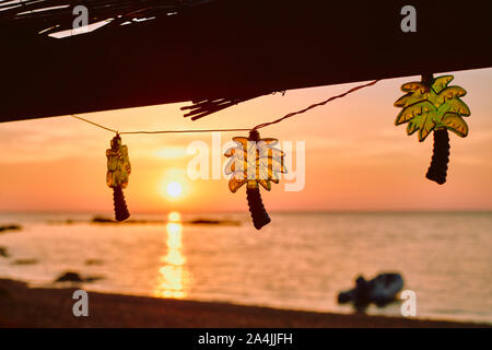 Palm tree a forma di stringa di festa luci decorare un rustico bar sulla spiaggia cafe con un tramonto cielo e mare spiaggia sfondo - tropical beach holiday Foto Stock