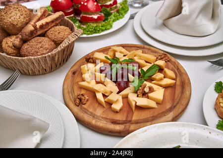 Piccoli pezzi di formaggio di diverse varietà giacciono su di un piatto di legno su una tavola servita nel ristorante. Foto Stock