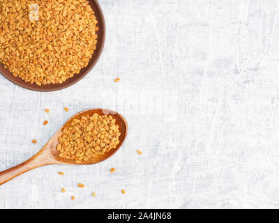 Spezie ed erbe contribuiscono a mantenere in buona salute e a migliorare l'appetito, vista dall'alto su sfondo di calcestruzzo. Fenugreek nella piastra di argilla e il cucchiaio di legno. Moderno Foto Stock