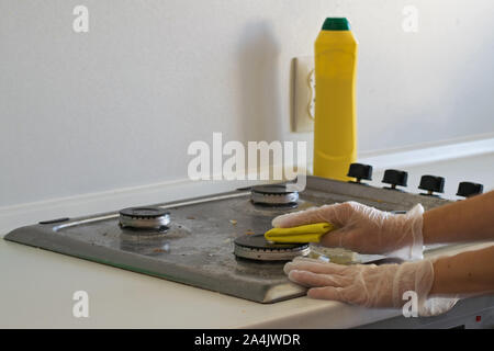 Una mano umana in un guanto di gomma bianca lava la stufa a gas con un detergente. Foto Stock