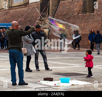 Bologna / Italia - 12 Ottobre 2019: Street performer rende grandi bolle di sapone in Piazza del Nettuno di Bologna, Italia. I bambini raccogliere felice intorno a lui. Foto Stock