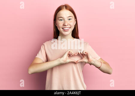 Close up ritratto di positivo affascinante ragazza ragazzo dando il suo cuore isolato sfondo rosa, donna che fa il gesto di cuore, il linguaggio del corpo. La felicità Foto Stock