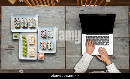 Consegna qualche piatto di sushis e portatile su due tavoli in legno Foto Stock