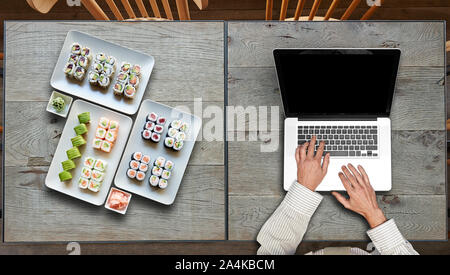 Consegna qualche piatto di sushis e portatile su due tavoli in legno Foto Stock