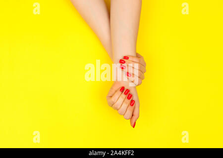 Giovane e bella donna di mano con perfetta manicure rosso su sfondo giallo. Piatto stile di laici. Foto Stock