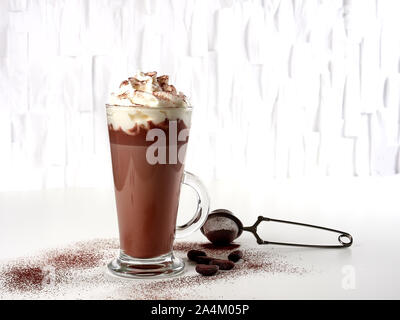 Cioccolata calda latte con panna montata, nel bicchiere alto, sprinked con polvere di cacao, su sfondo bianco Foto Stock