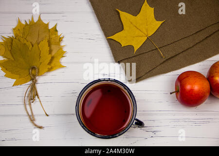 Il tè in una tazza bianca con zucchero bianco tagliato a cubetti e lo zucchero di canna, foglie di acero e mele su una tavola di legno sfondo luminoso. Foto Stock