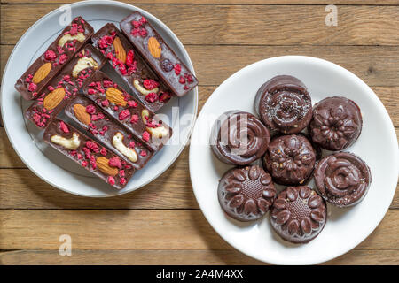 In casa vegan dolci crudo su bianco piattini su un tavolo di legno. Trattare sano per il tè in background. Bastoni e caramelle con cioccolato naturale, di lamponi Foto Stock