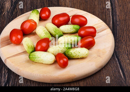 Fresche e mature poco cetrioli e pomodori ciliegia su un tagliere di legno. Stile rustico. Foto Stock